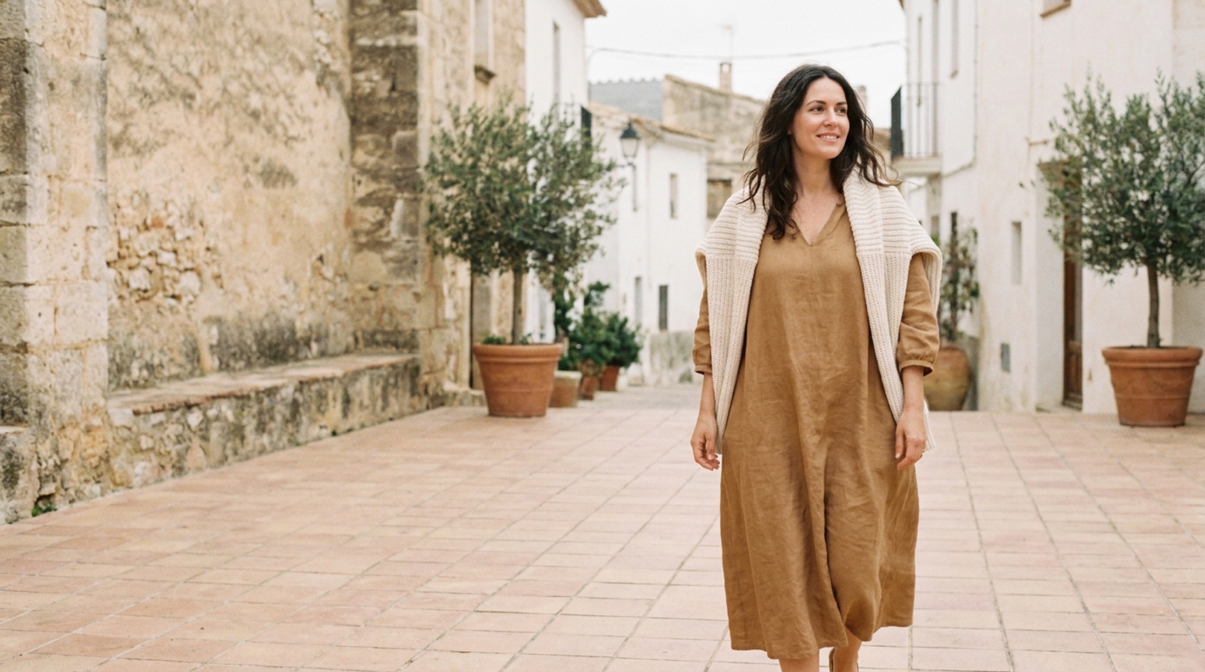 Mujer con vestido midi de lino camel caminando por un patio mediterráneo